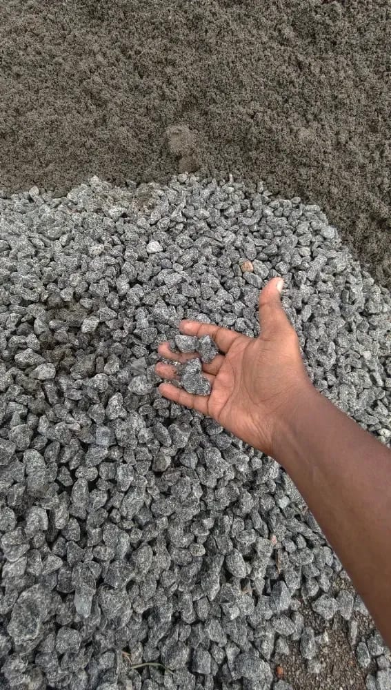 A handful of blue metal jelly held over a delivered heap, next to M-sand, at a customer's site